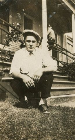 Orville W Garrison squatting by porch stairs cigarette in hand